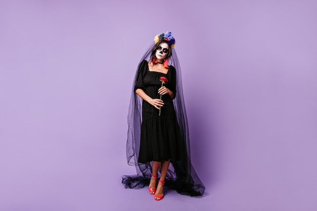 Veuve mexicaine tristement, tenant une rose rouge. Photo pleine longueur d'une femme en tenue noire avec voile de mariée.
