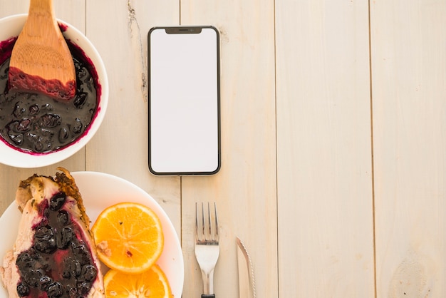 Viande avec de la confiture près des oranges et smartphone