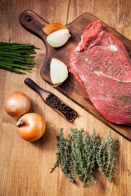 Viande crue de la boucherie sur planche de bois avec des ingrédients. Oignons crus. Herbes vertes.