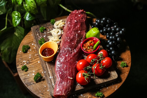 Viande crue salée sur la planche de bois avec légumes champignons sauce tomate poivron vue côté raisin