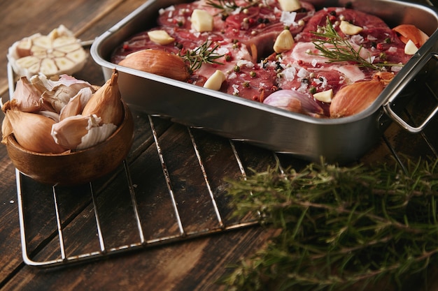 Photo gratuite viande dans une poêle en acier avec des épices autour: ail, romarin, oignons; prêt à cuire sur le côté de la table en bois brossé grunge épais