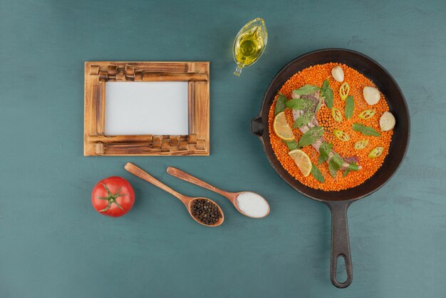 Viande non cuite avec lentilles rouges, tranches de poivre, ail et épinards dans une poêle noire avec cadre photo et huile.