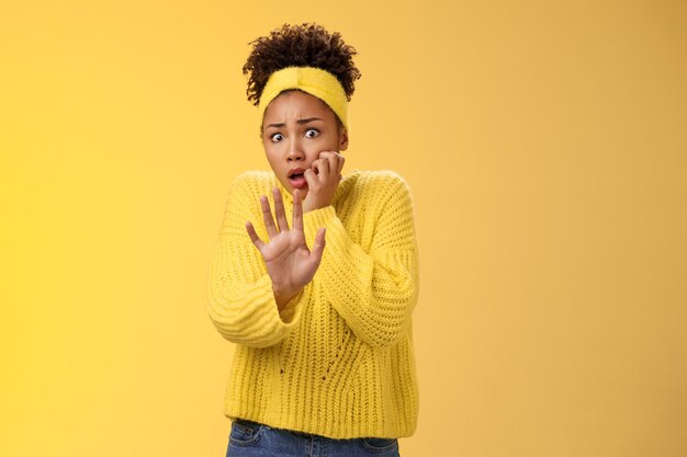 Une victime terrifiée effrayée par les abus a l'air effrayée d'étendre le bras suppliant de ne pas blesser s'approcher élargir les yeux se ronger les ongles haletant choqué debout abasourdi effrayé, horrifié mur jaune.