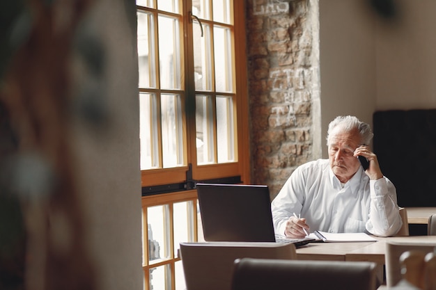 Vieil homme assis à la table et travaillant avec un ordinateur portable