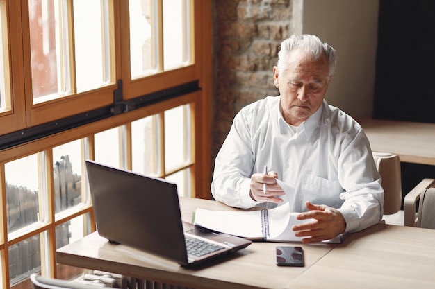 Vieil homme assis à la table et travaillant avec un ordinateur portable