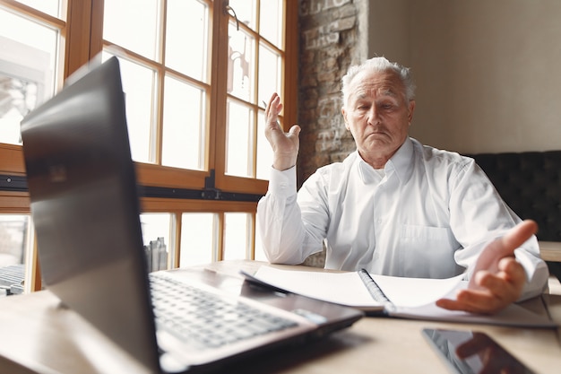 Vieil homme assis à la table et travaillant avec un ordinateur portable