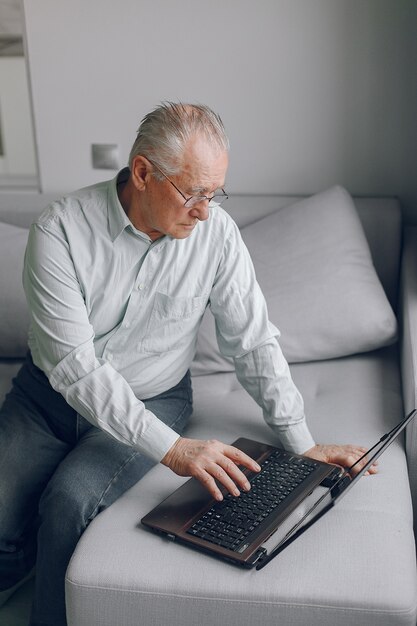 Vieil homme élégant assis à la maison et à l'aide d'un ordinateur portable