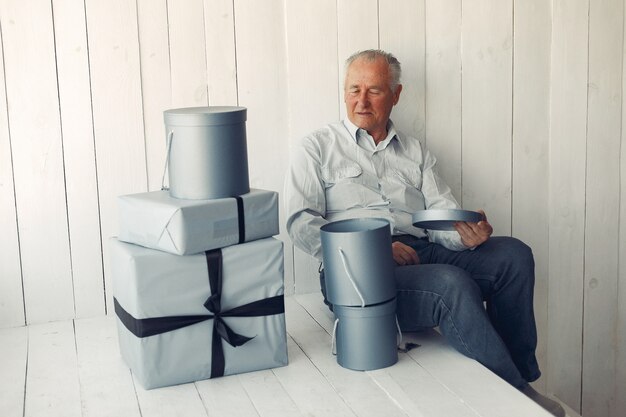 Vieil homme élégant assis à la maison avec des cadeaux de Noël