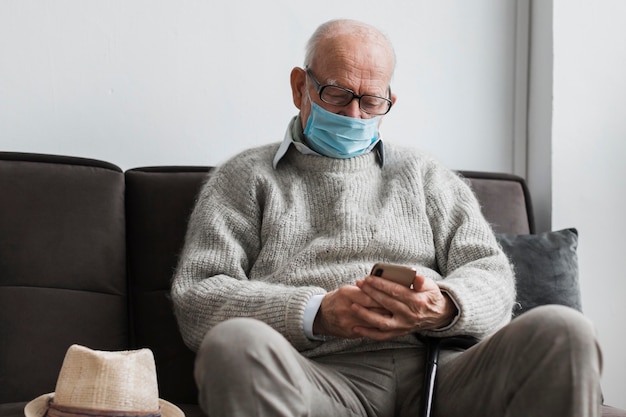 Vieil homme avec masque médical dans une maison de soins infirmiers à l'aide de smartphone