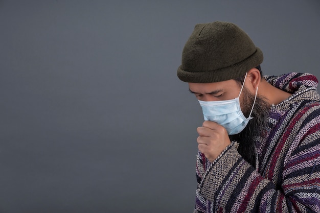 Vieil homme porte un masque en toussant sur le mur gris.