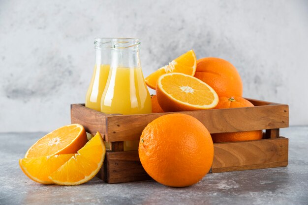 Une vieille boîte en bois pleine de fruits orange et de pichets en verre de jus sur table en pierre.