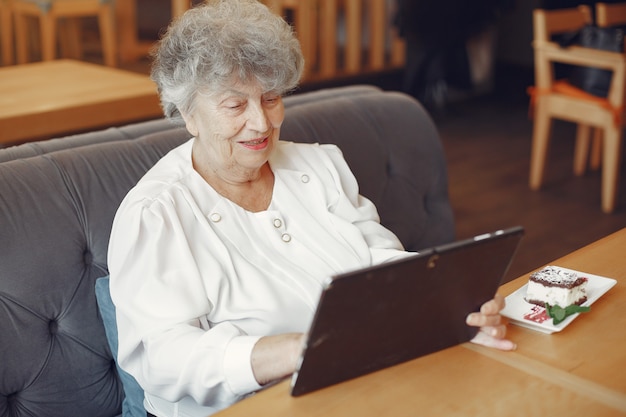 Vieille femme élégante assise dans un café et à l'aide d'un ordinateur portable