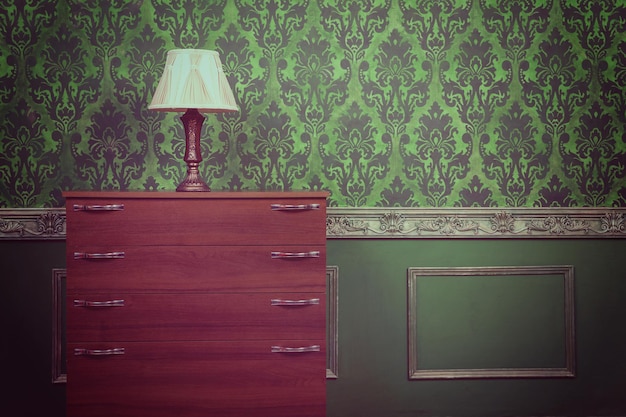 Vieille lampe rétro dans un intérieur vintage sur des meubles dans une chambre avec des murs à motif rococo