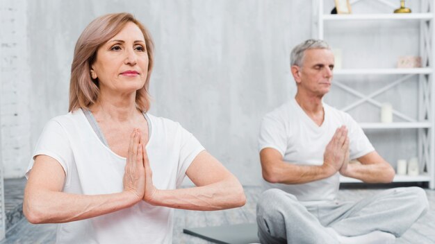 Vieux couple en bonne santé, assis en posture de lotus avec les mains en prière