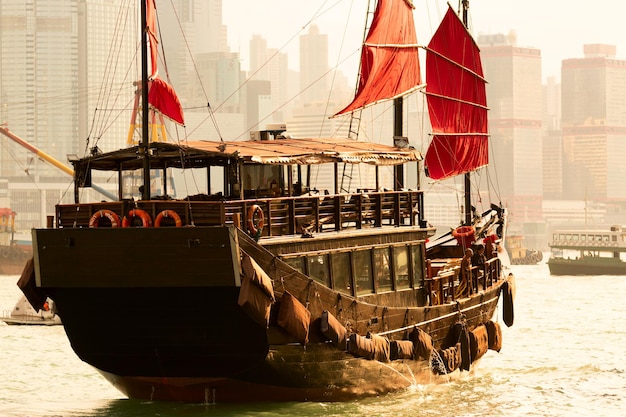 Vieux ferry touristique en bois dans le port de victoria contre la célèbre vue sur l'île de hong kong avec des gratte-ciel