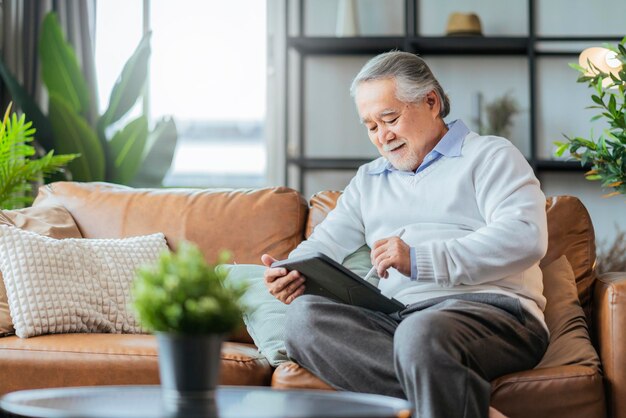 Un vieux grand-père senior asiatique profite du week-end du dimanche en lisant un cahier sur un canapé-lit à la maison.