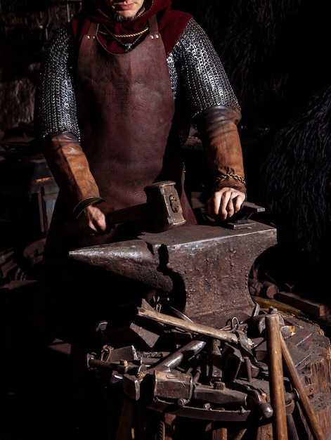Photo gratuite viking forge des armes et des épées dans la forge. un homme en habit de guerrier est dans la forge.