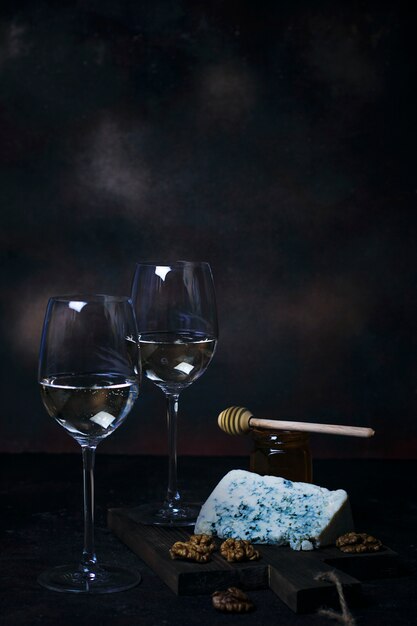 Vin blanc en verre fin avec du fromage bleu, miel, noix sur fond noir