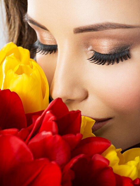 Visage de beauté gros plan de la jeune femme avec des fleurs. Modèle attrayant avec des tulipes rouges et jaunes