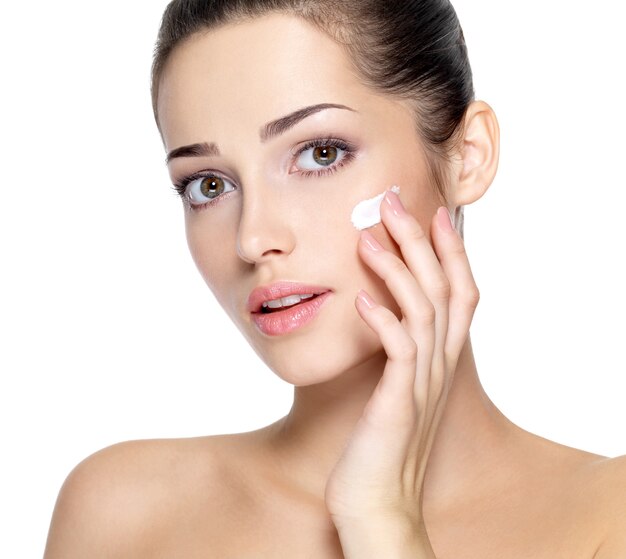 Visage beauté de la jeune femme avec une crème cosmétique sur une joue. Concept de soins de la peau. Closeup portrait isolé sur blanc.