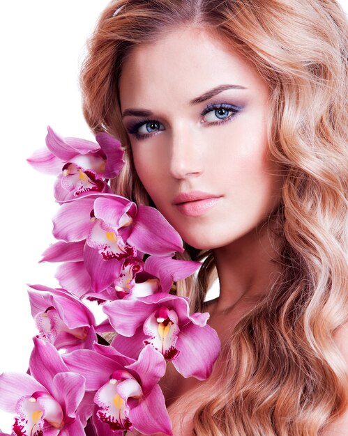 Visage de belle femme avec une peau saine et fleur rose sur un mur blanc.