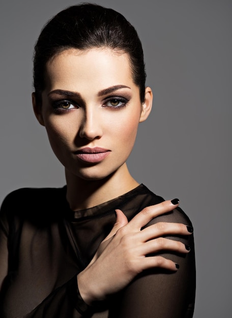 Visage d'une belle fille avec du maquillage de mode et des ongles noirs posant sur un mur sombre