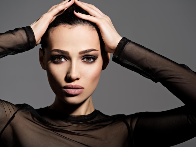 Visage d'une belle fille avec le maquillage des yeux charbonneux posant sur un mur sombre