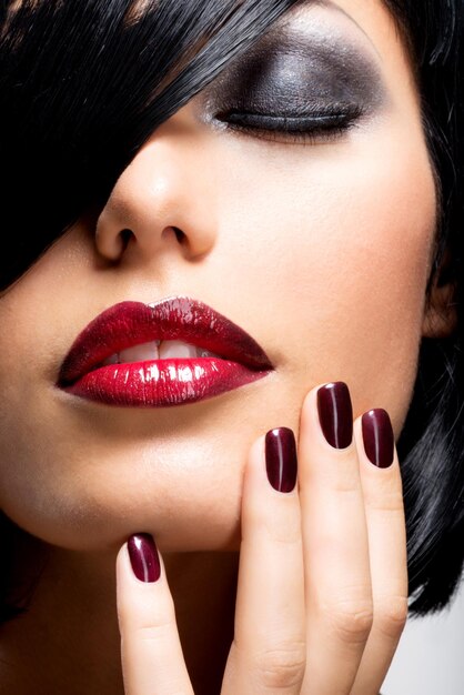 Visage d'une femme avec de beaux ongles foncés et des lèvres rouges sexy. Mannequin aux cheveux noirs