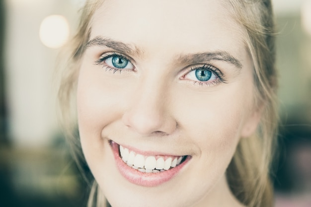 Visage d'heureuse belle jeune femme blonde aux yeux bleus et aux dents blanches