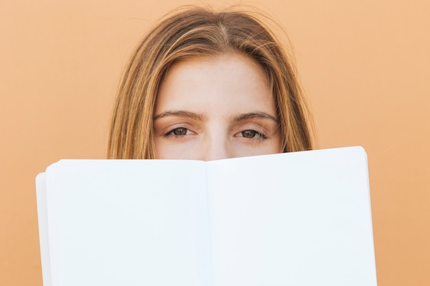 Photo gratuite visage de jeune femme blonde avec un livre blanc sur la bouche