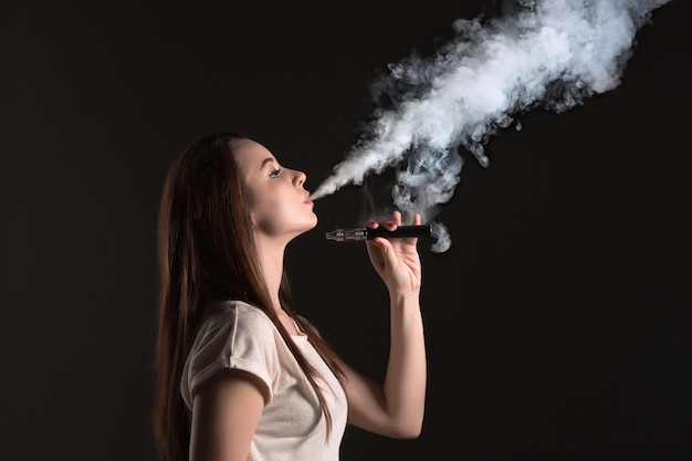 Le visage de la jeune femme vaping au studio noir