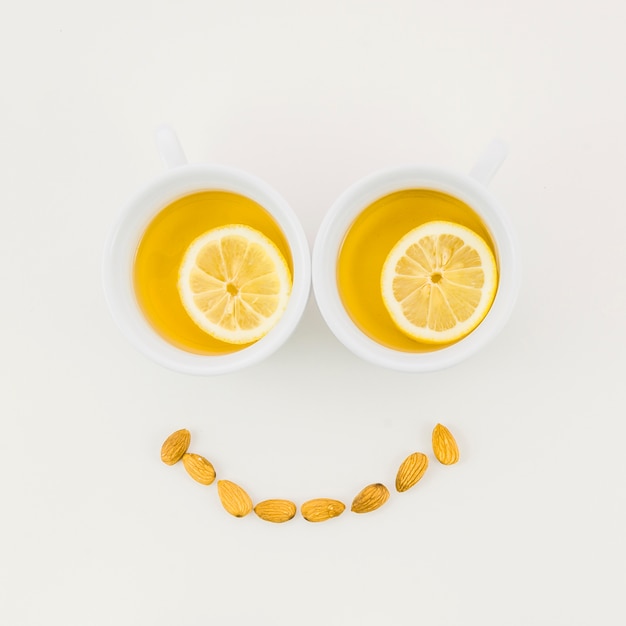 Photo gratuite visage souriant fait avec une tasse de thé au citron et amandes isolées sur fond blanc