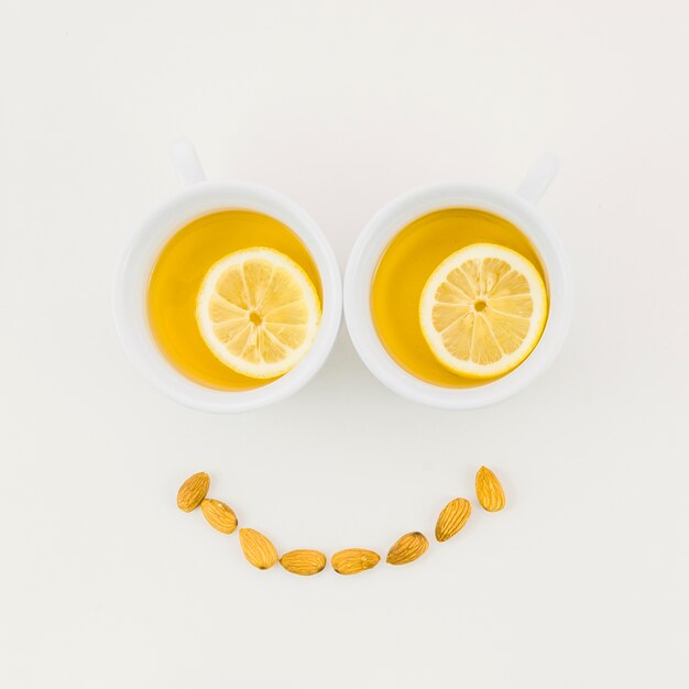 Visage souriant fait avec une tasse de thé au citron et amandes isolées sur fond blanc