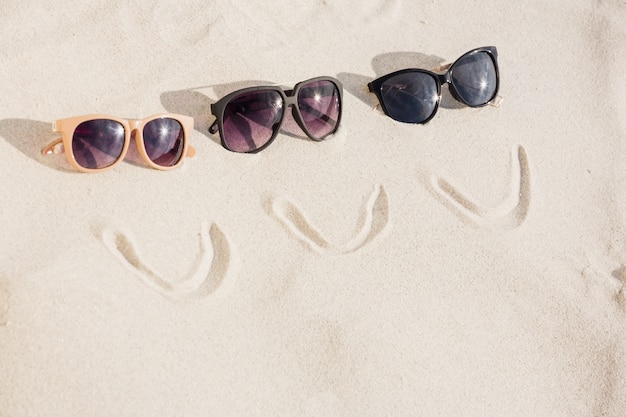 Visage souriant et trois lunettes de soleil sur le sable