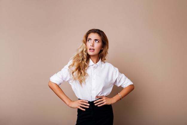 Visage surprise. Femme blonde en tenue décontractée debout sur un mur beige. Fille sortie à la recherche.