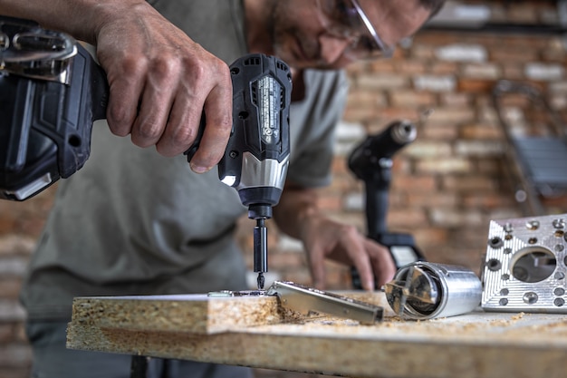 Vissage d'une vis autotaraudeuse dans un trou de fixation métallique sur une lame de bois à l'aide d'un tournevis, travail d'un menuisier.