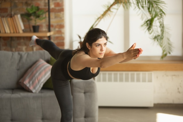 Vitalité. Belle jeune femme musulmane arabe et sportive prenant des cours de yoga professionnels en ligne et s'entraînant à la maison. Concept de mode de vie sain, bien-être, bien-être, passe-temps. Flexible et motivé.