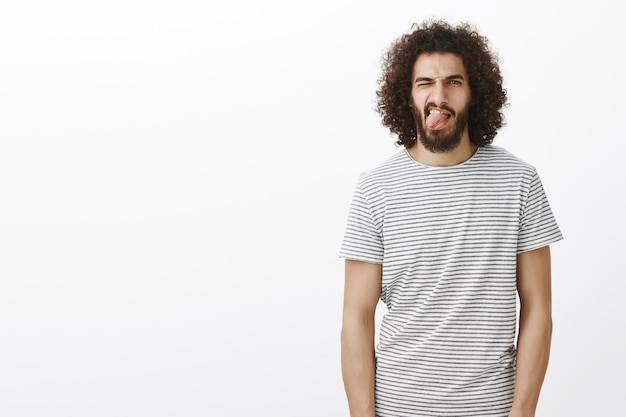 Vivez pleinement votre vie. Portrait de beau mâle insouciant avec barbe et cheveux bouclés, qui sort la langue et un clin de œil