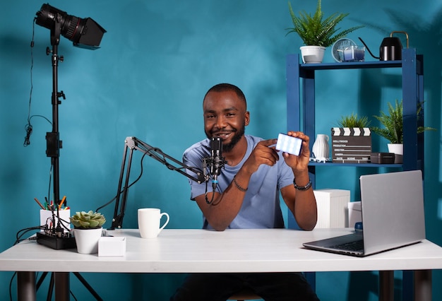 Vlogger présentant une petite revue de lumière vidéo rgb pointant sur les caractéristiques du produit assis au bureau dans un studio de vlogging. Influenceur examinant l'éclairage continu de la vidéographie portable à l'aide d'un microphone.