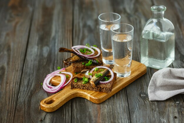 Vodka avec du poisson et du pain grillé sur table en bois
