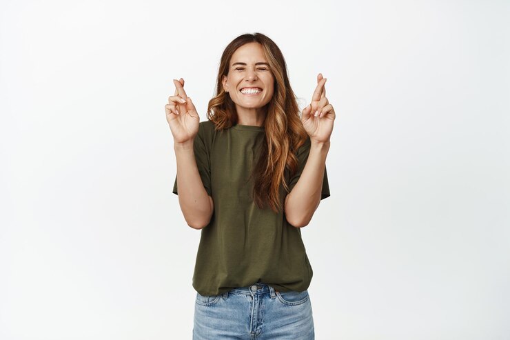 Photo gratuit vœux. une femme adulte souriante croise les doigts, ferme les yeux, pense positivement, souhaite que le rêve devienne réalité, espère atteindre le prix de l'objectif, debout excitée sur fond blanc.
