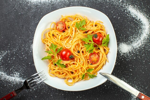 Voir ci-dessus des spaghettis végétaliens aux tomates et au vert sur une assiette de couverts en forme de carré sur fond de couleurs blanc noir