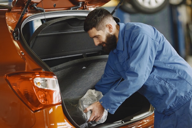 Voiture dans le garage. Guy en vêtements de travail. Barbe noire.