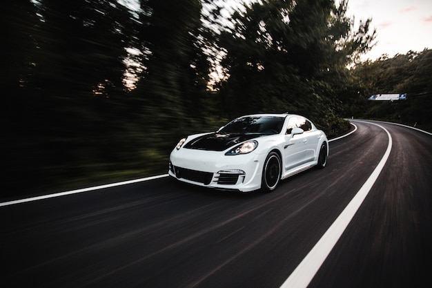 Une voiture de sport blanche avec autoréglage noir conduisant à grande vitesse sur la route.