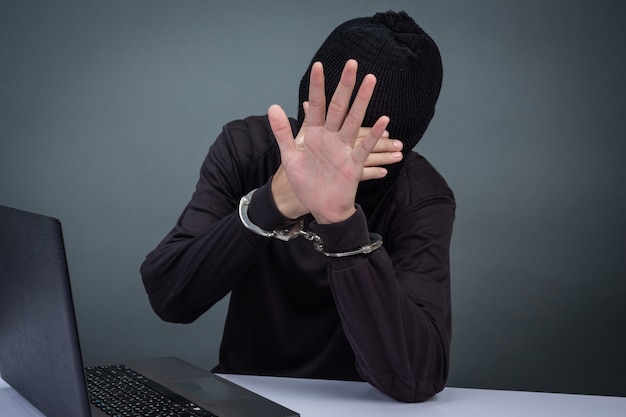 Photo gratuite voleur portant un chapeau noir, obscurcissant le visage, a été arrêté sur fond gris