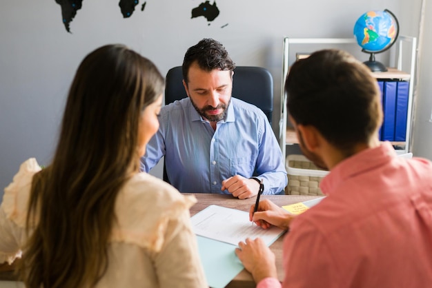 Photo gratuite vous avez un accord. jeune homme signant un contrat de vente pour des vacances avec sa femme. représentant commercial concluant un accord pour une vente en temps partagé avec certains clients de l'agence de voyages