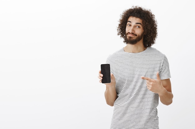 Vous regretterez si vous n'achetez pas de nouveau téléphone. Portrait de beau modèle masculin hispanique élégant avec barbe et cheveux bouclés