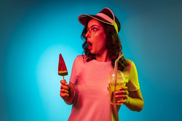 Vous vous demandez jeune femme dans une casquette tenant des bonbons et des boissons sur studio néon bleu branché