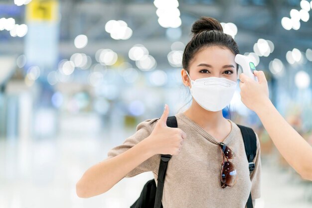 Voyage de sécurité nouveau mode de vie normalune voyageuse asiatique porte un contrôle de température en tissu décontracté détecte le covid19 au terminal de l'aéroport avant de partir à l'étranger voyage avec le terminal de départ de l'aéroport flou