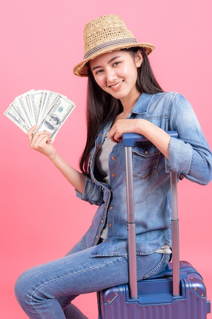 Voyageur de femme portant un chapeau de chalut est titulaire d'un passeport avec billet de banque et assis sur une valise.